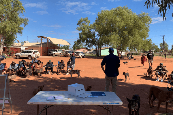 In an outdoor space, a table with a ballot box and people beyond it