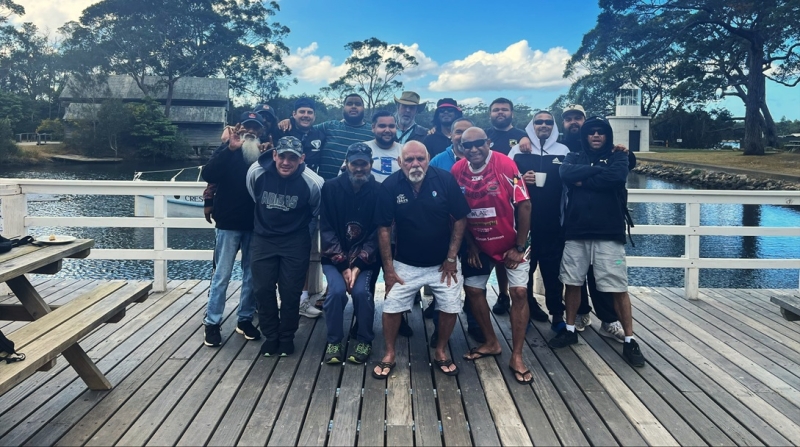 A group of men stands on a deck with water in the background