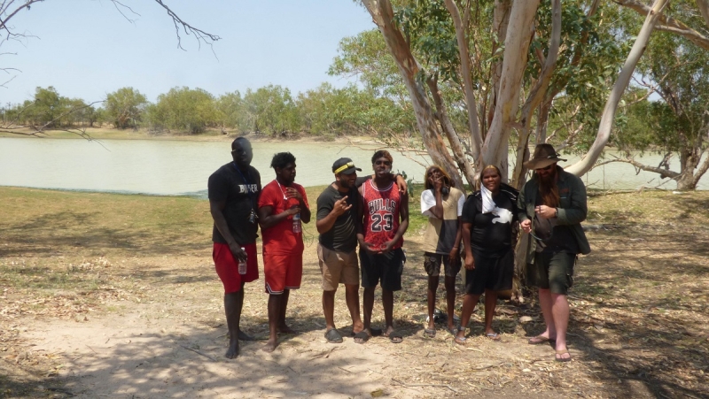 A group of people stand, smiling at the camera, with tress and a river behind them