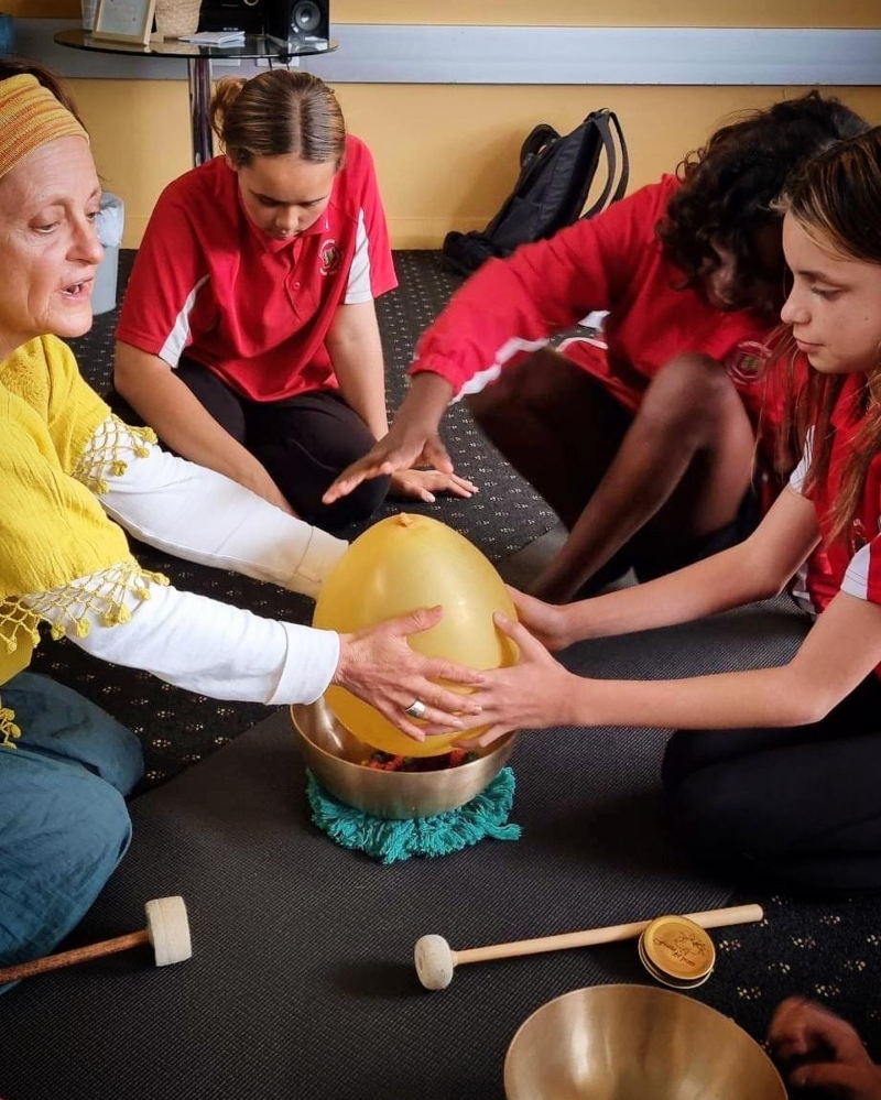 A woman and three young people sit on the floor with an orange egg-shaped object in the middle of them