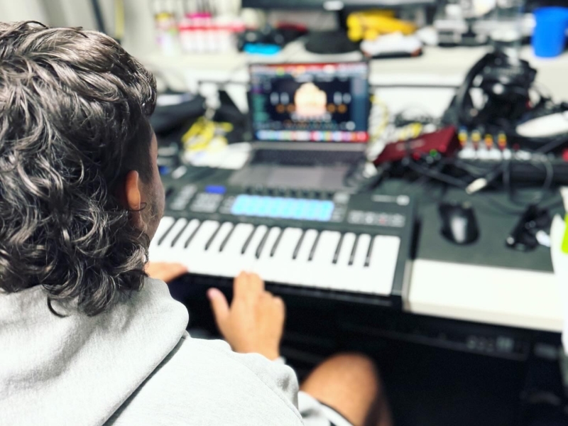 A person sits at an electronic keyboard with other recording equipment on the desk behind the keyboard