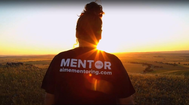 A person has their back to the camera. the back of their shirt reads MENTOR