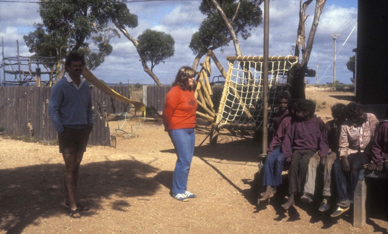 two people stand in an outdoor area talking to a small group of children