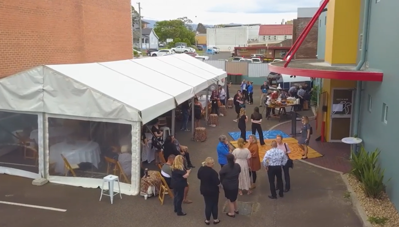 A high shot of a white temporary pavilion in a carpark with people walking nearby