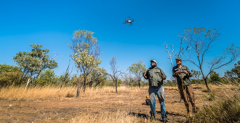 Two men fly a drone in an outdoor area