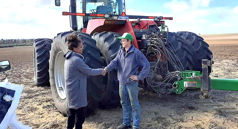 Two people shake hands while standing in front of large farm machinery