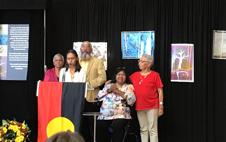 A young person speaks at a lectern with 4 adults standing behind her