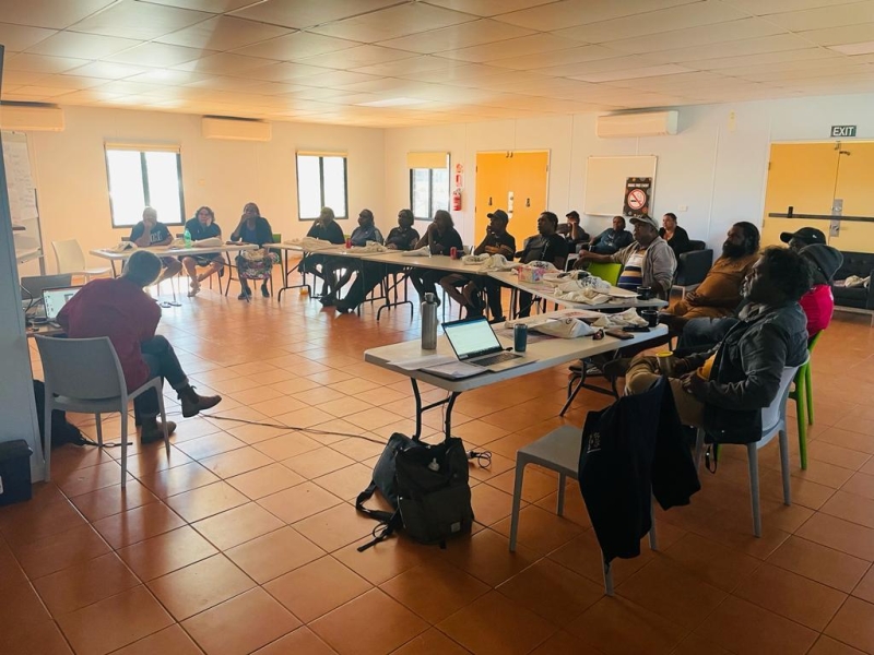 A group of people sit at tables arranged into a U shape with another person teaching in the middle of the U