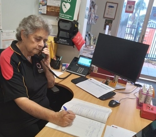 A woman sits at a desk holding a phone up to her ear