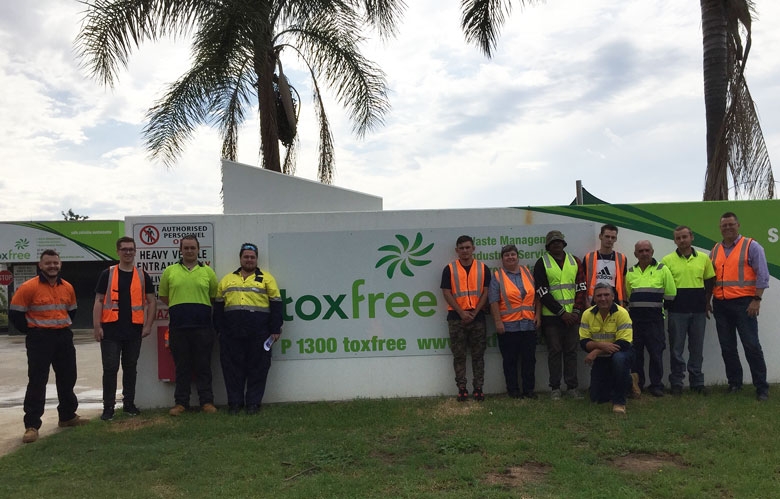 A group of people dressed in hi-vis pose outdoors around a sign that says toxfree