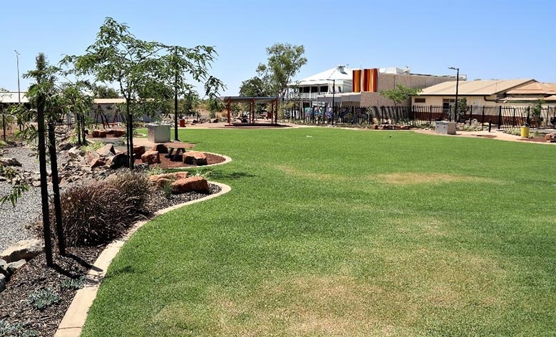 A green lawn with gardens to the left and buildings in the background