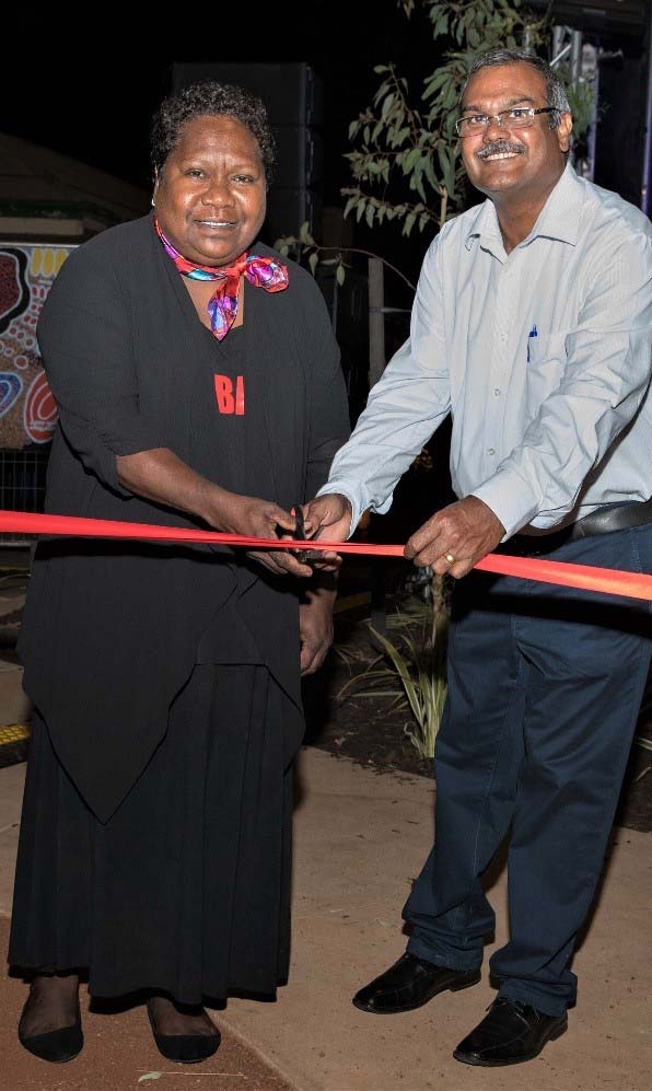 Two people smile at the camera as they cut a red ribbon