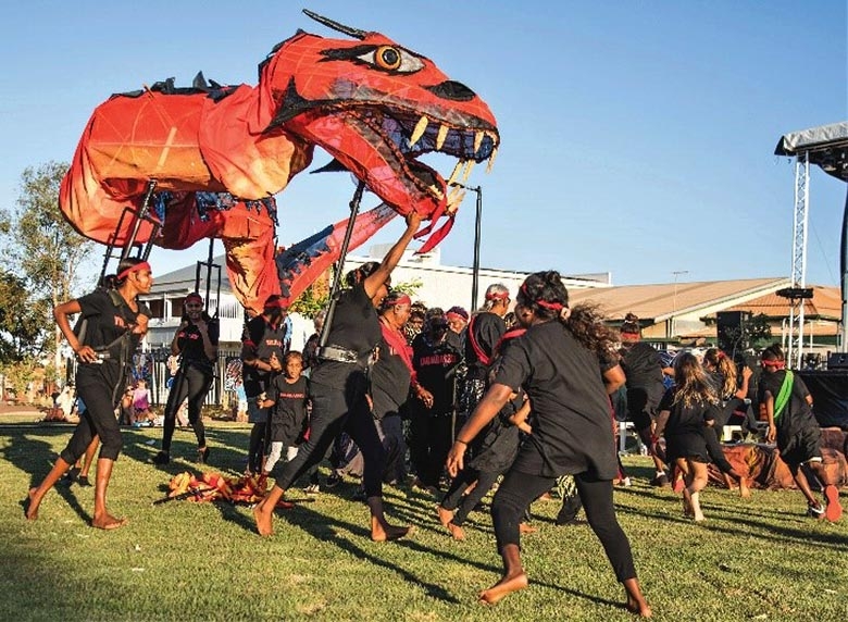 a large red dragon puppet is waved above the heads of a number of dancers dressed in black