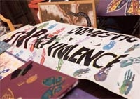 A hand-painted banner with handprints. The words 'domestic violence' can be seen