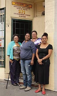 Four people stand outside a building with a sign saying 'Mudgin-Gal' above them
