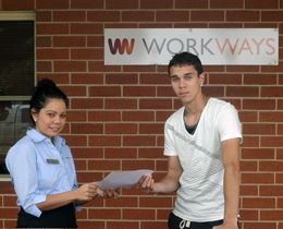 A woman handing a young man a piece of paper. On the wall behind them is a sign saying Workways