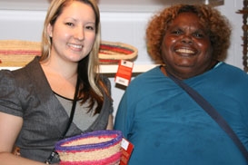 A smiling woman holds a woven pot. Another woman is smiling next to her