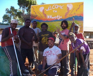A group of men under a sign saying welcome to Ngaanyatjarra