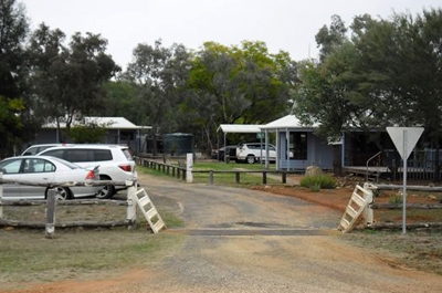 A driveway with cattle grid. Beyond it cars are parked and cabins can be seen