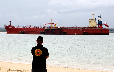A man stands on a beach looking at a large commercial ship
