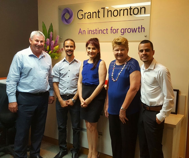 A group of people stand in an office with Grant Thornton on the wall