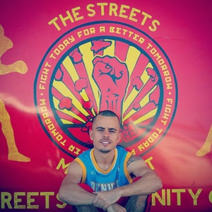 A man in front of a banner hat says 'The Streets: Fight today for a better tomorrow'
