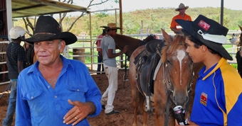 An older man and a younger man, with horses in the background