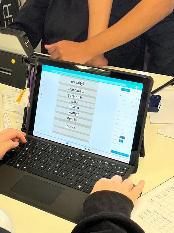 A laptop screen shows a number of words in an Aboriginal language