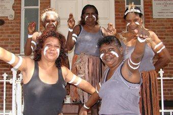 A group of women smile and pose for the camera. They have traditional paint markings on their faces and arms