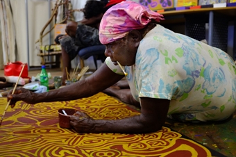 A woman leans over a large painting as she paints on it