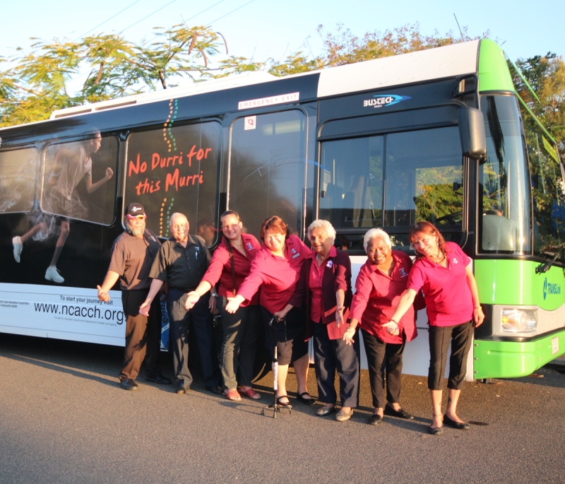 Seven people pose in front of a bus. the words No durri for this murri can be seen written on the bus window