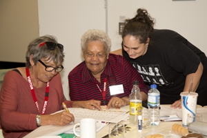 Three people lean over papers on a table