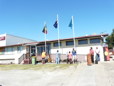 Three flag poles with the Australian, Aboriginal and Torres Strait Islander flags. Several people are at the foot of the poles