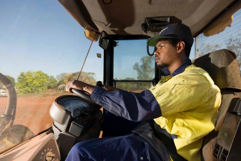 A young person wearing hi vis clothing and sitting in the driver's seat of a truck