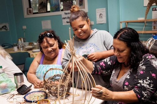 Three women work on weaving a basket