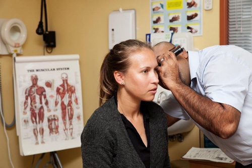 A woman sits in a doctor's office while a person looks into her ear