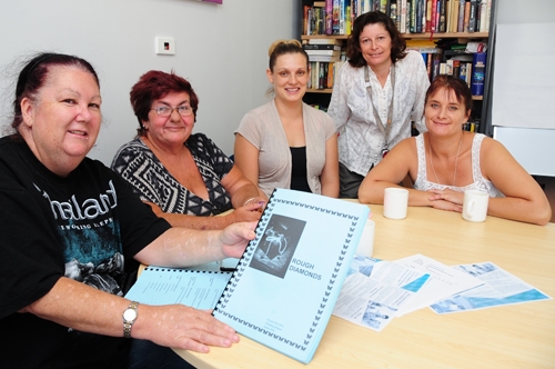 A group of women around a table. One is holding up a document