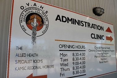 A sign on the wall of a building showing directions to different parts of the clinic, along with opening hours
